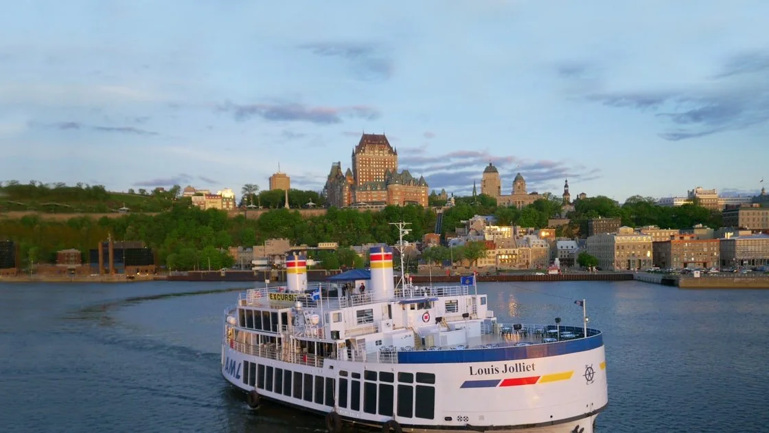 A white river cruise boat on the St. Lawrence in evening light, with the Château Frontenac and Old Québec on the bank behind
