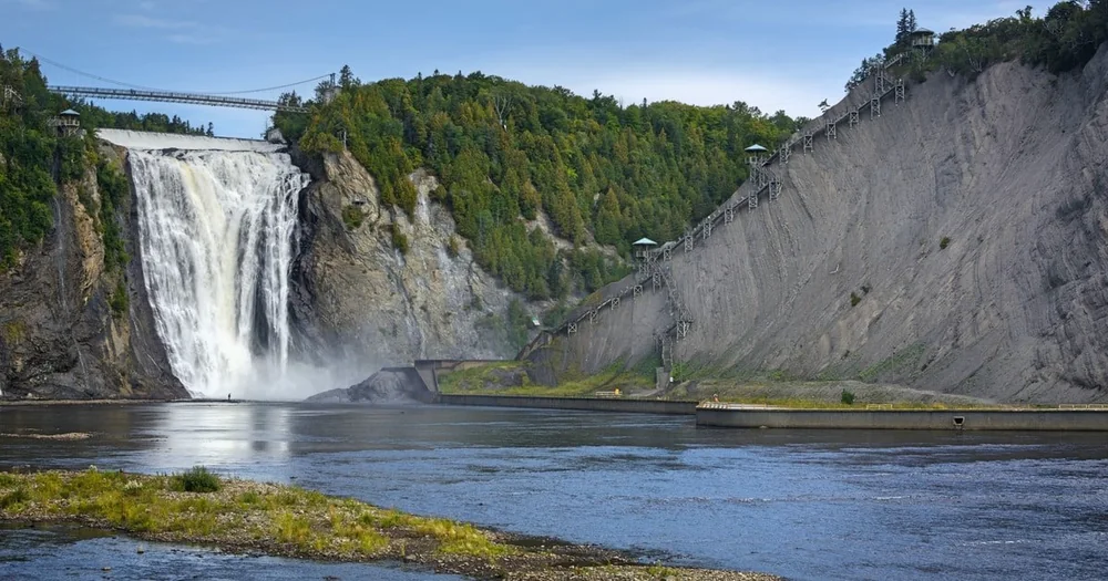 Montmorency Falls dropping into the river basin beside a bare grey slope, with the footbridge across the top