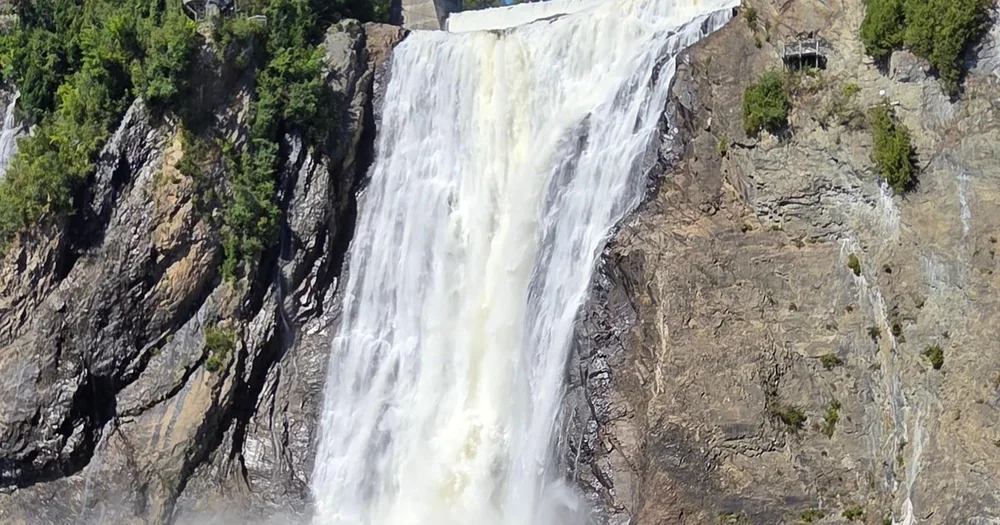 The full height of Montmorency Falls beside a sheer rock face on a sunny day