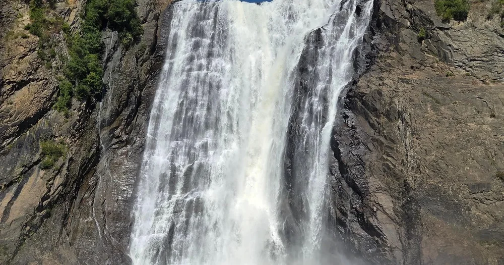 Close view of the white water curtain of Montmorency Falls against dark wet rock