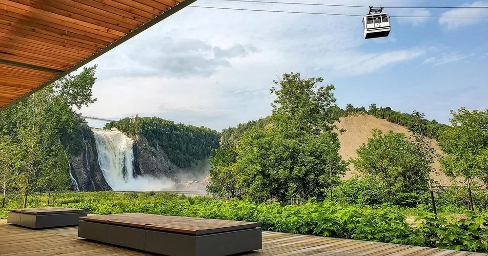 A wooden terrace with benches and greenery, with the falls and a cable car cabin in the distance